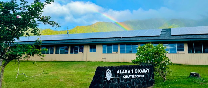 AOK school building in the forefront with a rainbow in the sky in the background