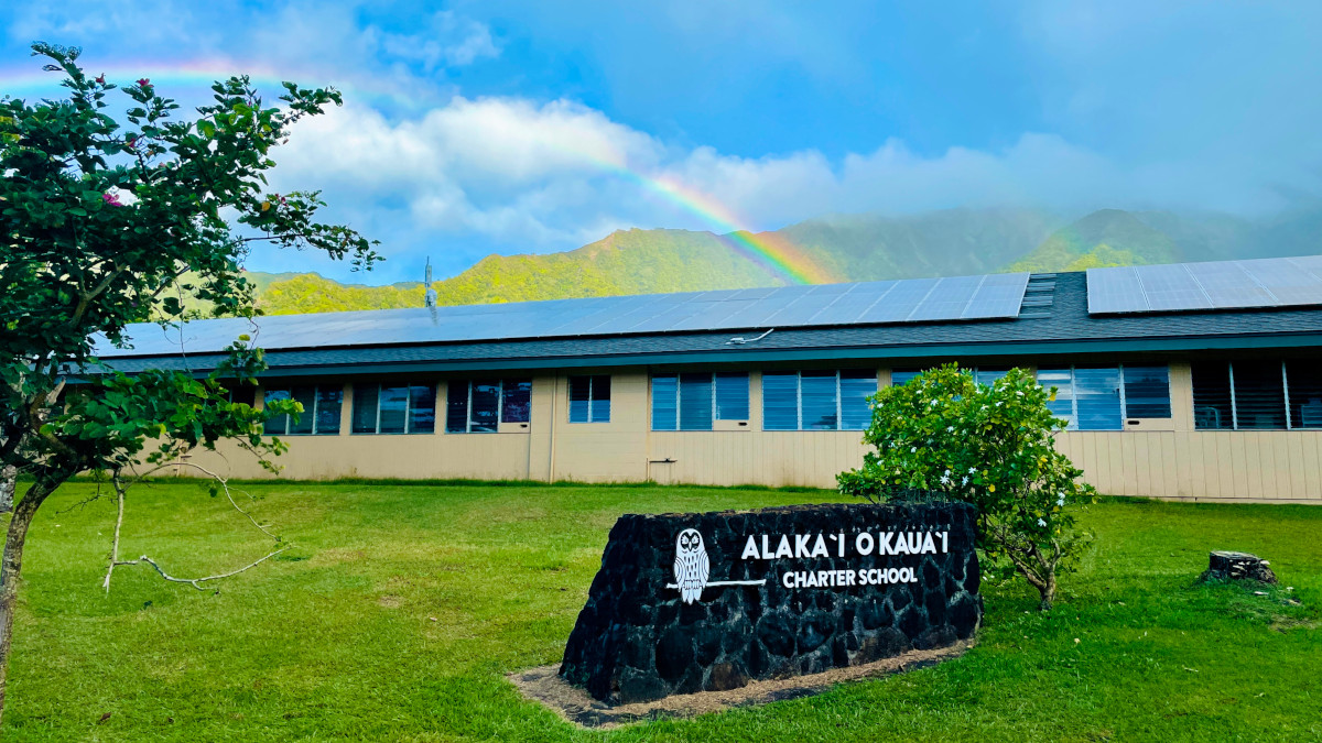 AOK school building in the forefront with a rainbow in the sky in the background