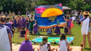 AOK learners holding up a colorful large painting of a sunset