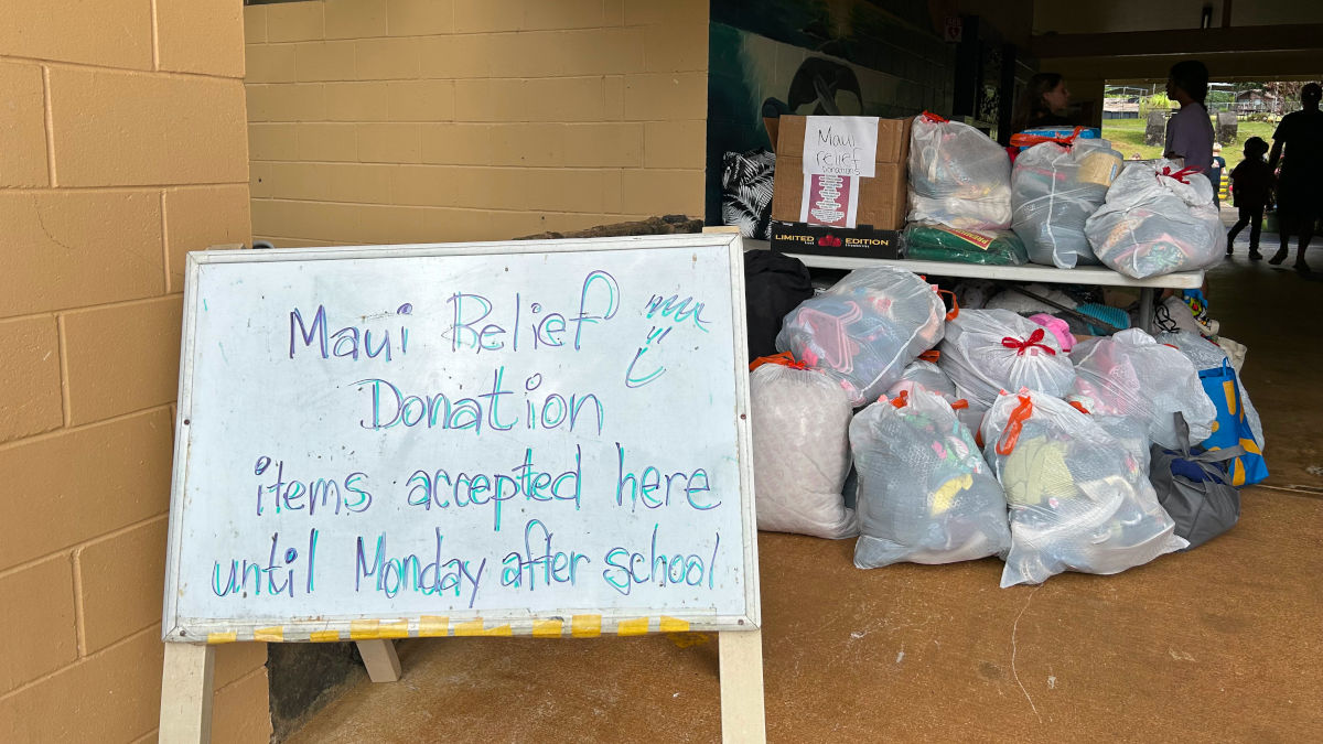 white board with a message about Maui Donation Relief and several full bags of donations in the background